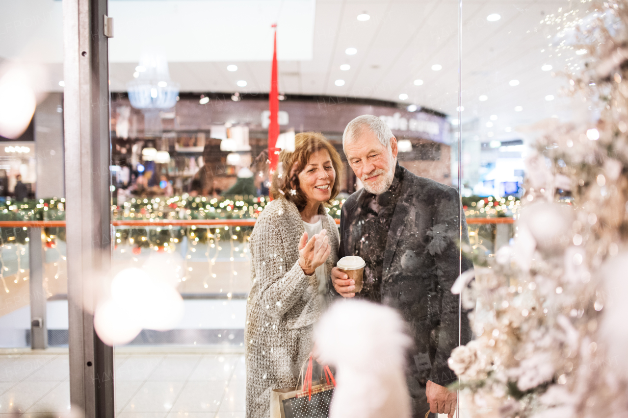 Senior couple doing Christmas shopping. Shopping center at Christmas time. Shot through glass.