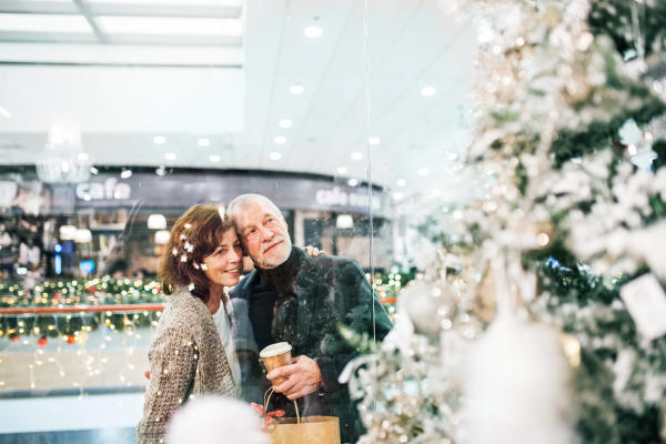 Senior couple doing Christmas shopping. Shopping center at Christmas time. Shot through glass.