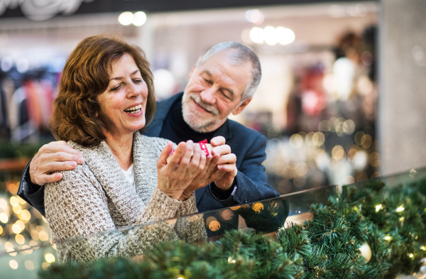 A portrait of senior couple holding a wrapped present in shopping center at Christmas time.