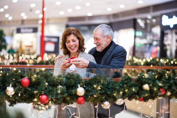 Senior couple doing Christmas shopping. A man giving a present to a woman. Shopping center at Christmas time.