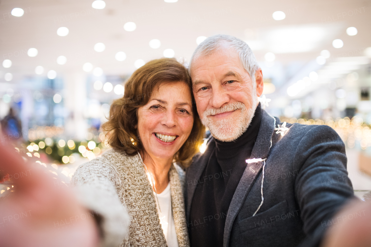 Happy senior couple taking selfie in shopping center at Christmas time.