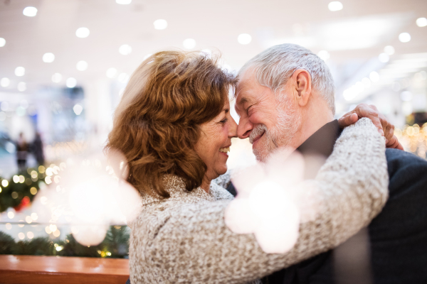 Senior couple doing Christmas shopping. Man and woman hugging. Shopping center at Christmas time.