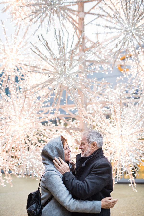 A waist up portrait of senior couple standing outdoors in front of shopping center at Christmas time. Copy space.