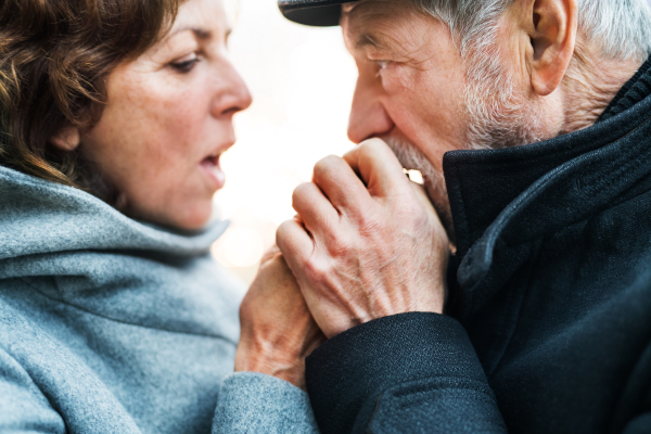 A close-up of senior couple standing outdoors, warming up hands when feeling cold.