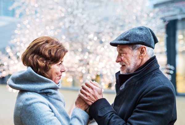 Senior couple looking at each other in shopping centre at Christmas time, holding hands.