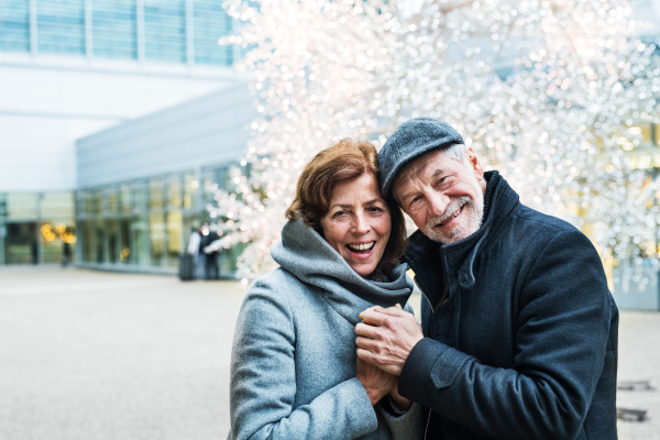 A waist up portrait of senior couple standing outdoors in front of shopping center at Christmas time. Copy space.