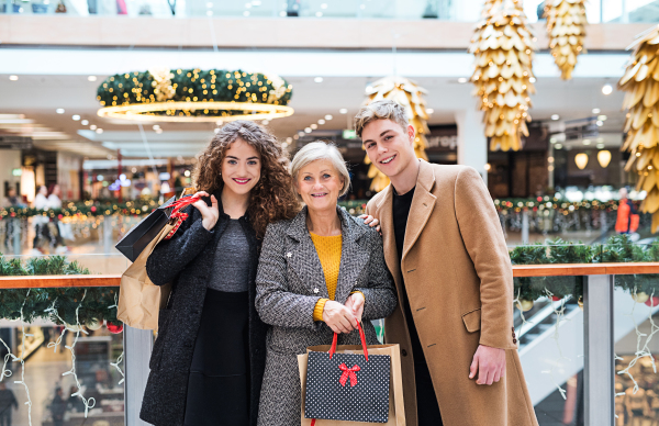 A portrait of senior grandmother and teenage grandchildren with paper bags standing in shopping center at Christmas time.