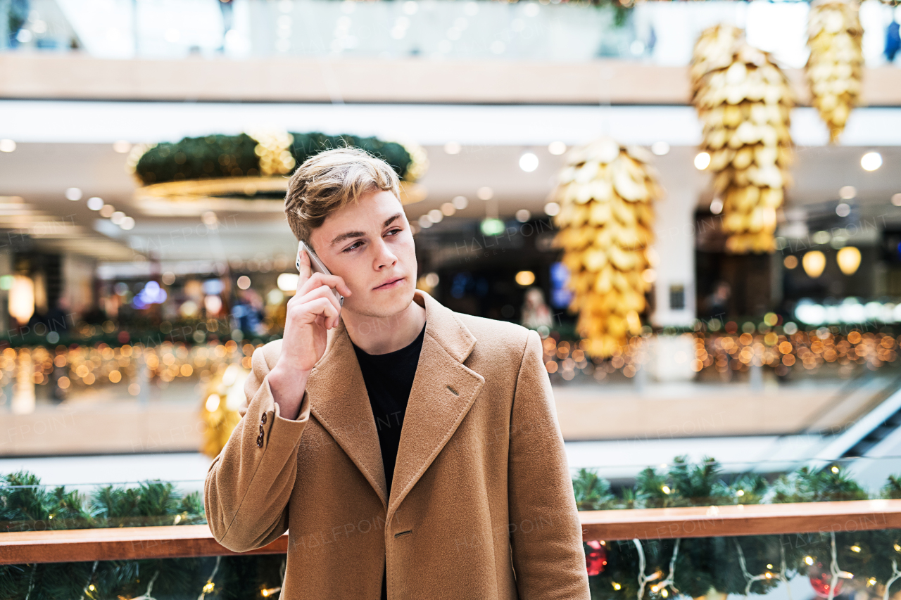 A portrait of teenage boy with smartphone in shopping center at Christmas, making a phone call.