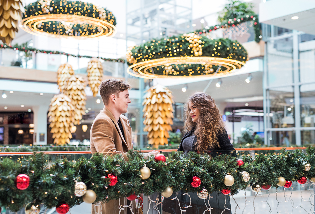 A happy young couple looking at each other in shopping center at Christmas time.