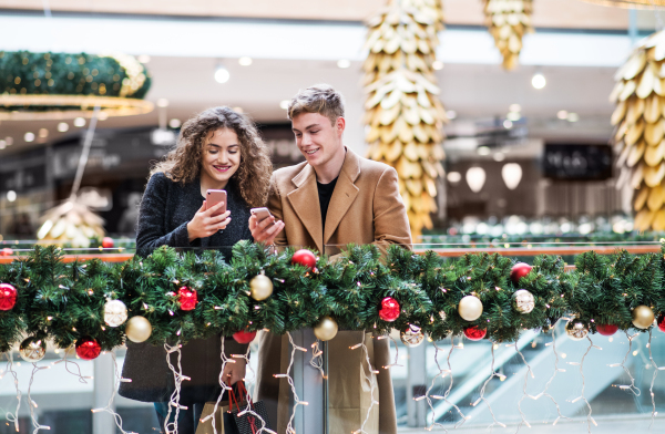 A happy young couple with smartphone in shopping center at Christmas time, text messaging.