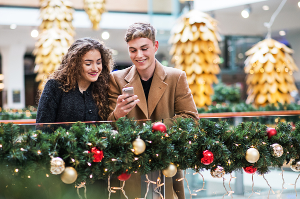 A happy young couple with smartphone in shopping center at Christmas time, text messaging.