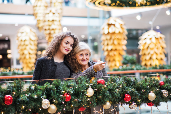 A portrait of senior grandmother and teenage granddaughter standing in shopping center at Christmas time, pointing to something.