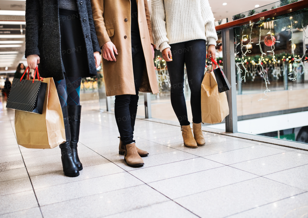 Unrecognizable young friends with bags walking in shopping center at Christmas time.