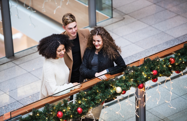 A high-angle view of young friends standing in shopping center at Christmas time.