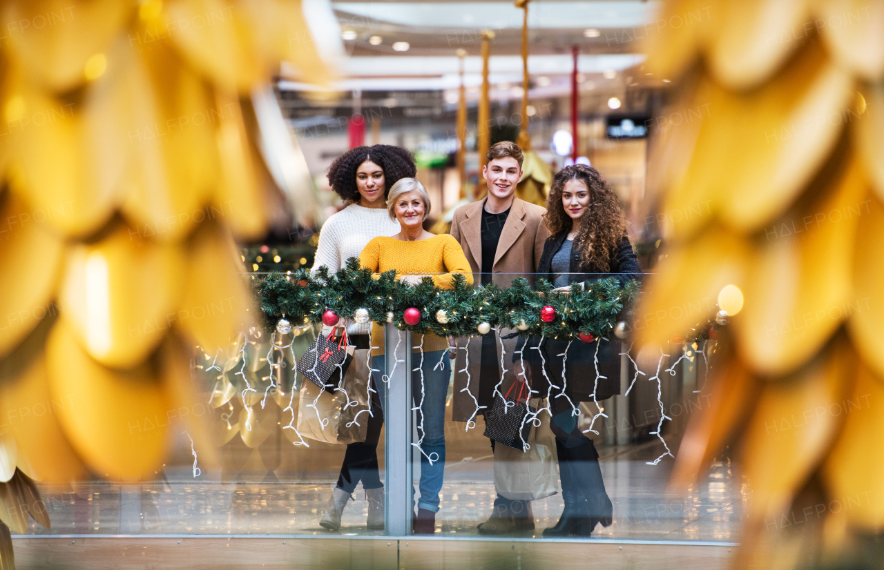 A portrait of senior grandmother and teenage grandchildren with paper bags standing in shopping center at Christmas time.