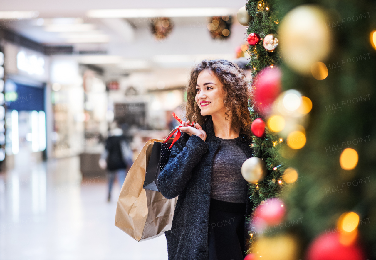 A portrait of happy teenage girl with paper bags in shopping center at Christmas. Copy space.