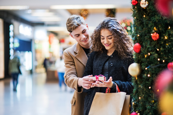 A happy young man giving a present to his girfriend in shopping center at Christmas time. Copy space.