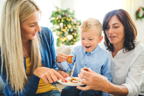 A small boy with mother and grandmother sitting on the sofa at home at Christmas time, eating biscuits.