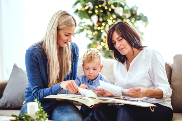 A small boy with mother and grandmother sitting on the sofa at home at Christmas time, looking at photos.