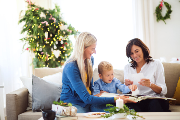 A small boy with mother and grandmother sitting on the sofa at home at Christmas time, looking at photos.