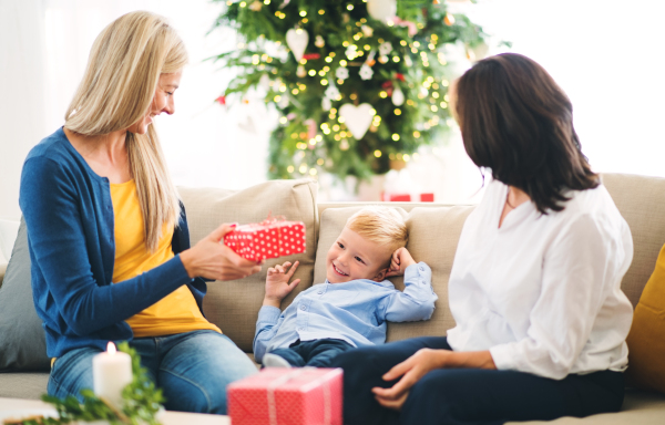 A mother and grandmother giving presents to a happy small boy at home at Christmas time.