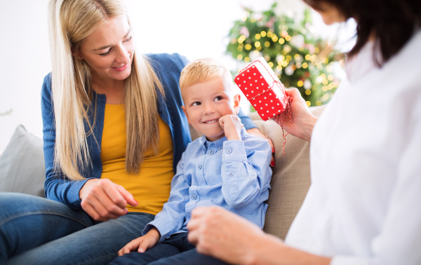 A mother and unrecognizable grandmother giving presents to a happy small boy at home at Christmas time.