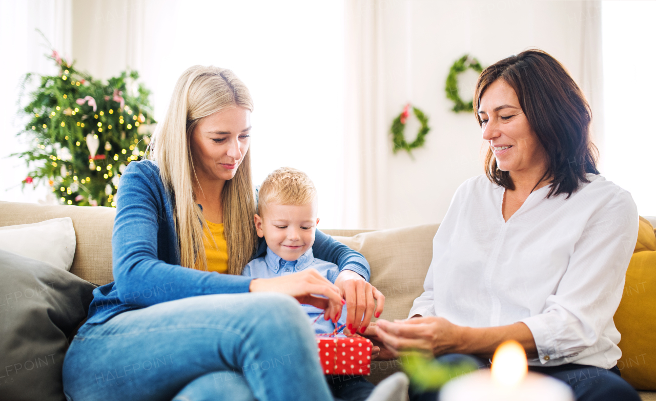 A small boy with mother and grandmother wrapping or opening a present at home at Christmas time.