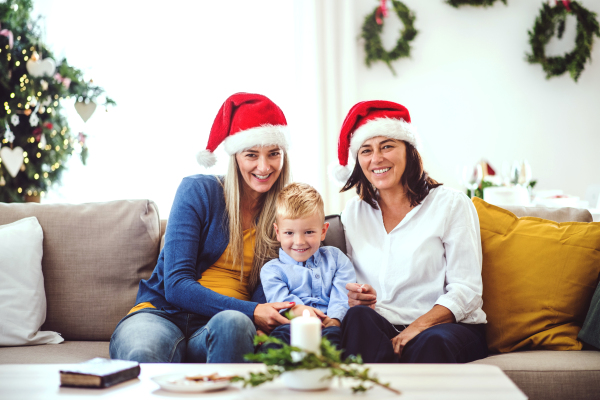 A small boy with mother and grandmother with Santa hat sitting on a sofa at home at Christmas time.