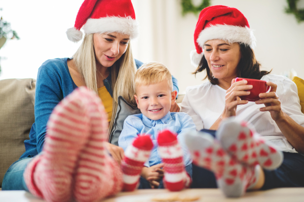 A small boy with mother and grandmother with Santa hat sitting on a sofa at home at Christmas time.