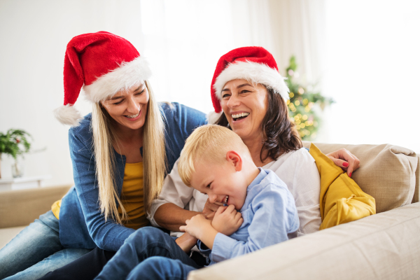 A small boy with mother and grandmother with Santa hat sitting on a sofa at home at Christmas time, having fun.