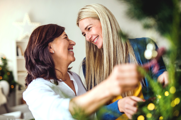 A happy senior woman with adult daughter standing by Christmas tree at home.