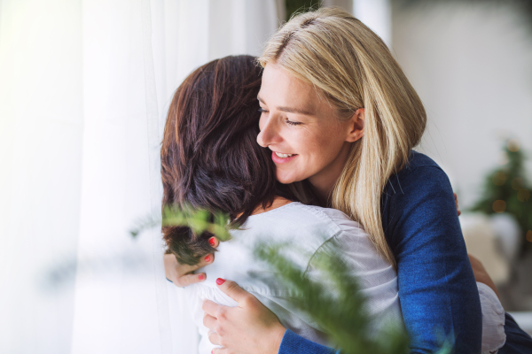 A senior woman with adult daughter at home at Christmas time, hugging.