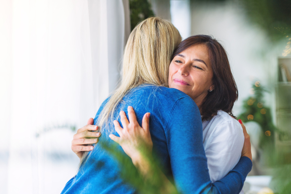 A senior woman with adult daughter at home at Christmas time, hugging.