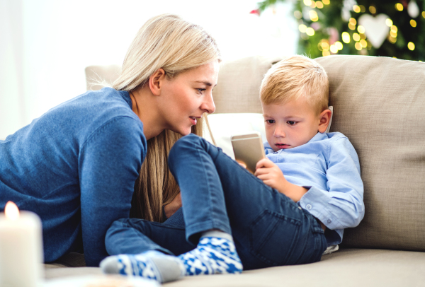 A mother and small boy with smartphone sitting on a sofa at home at Christmas time, playing games.