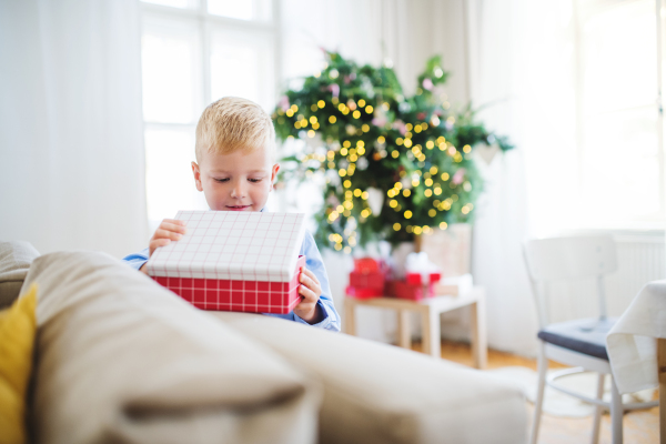 A small boy standing by a sofa at home at Christmas time, opening up a present.