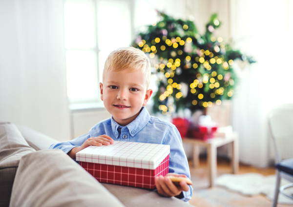 A small boy with a present standing at home at Christmas time.