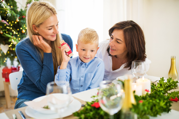 A small boy with present and mother and grandmother sitting at a table at home at Christmas time.