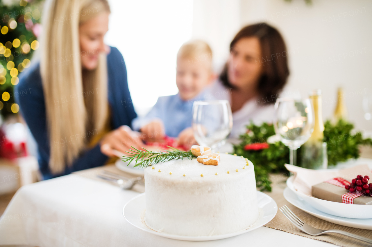 A white a cake on table set for dinner at Christmas time, a family in the background.