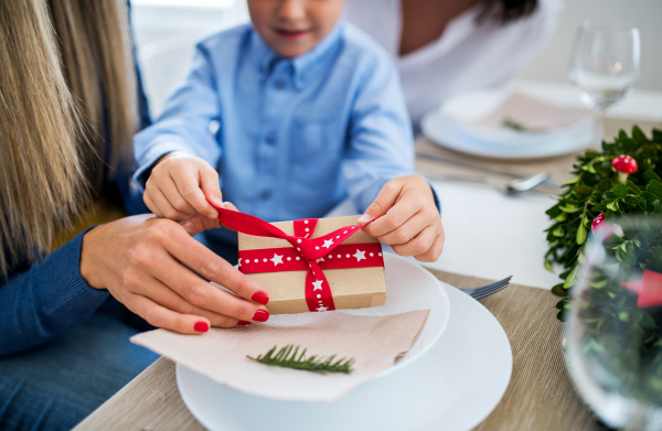 An unrecognizable small boy with present and mother sitting at a table at home at Christmas time.