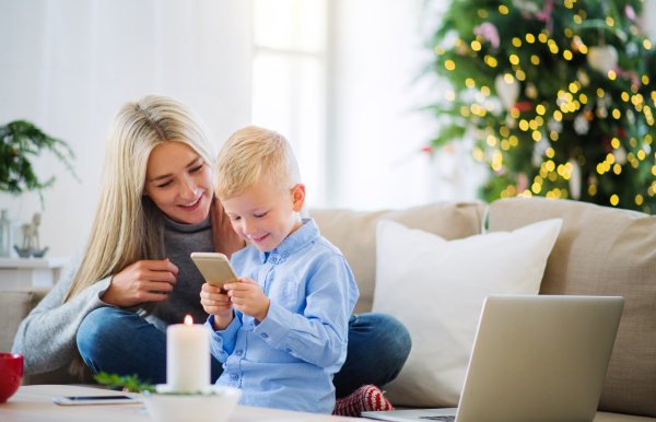 A mother and small boy with smartphone sitting on a sofa at home at Christmas time, playing games.