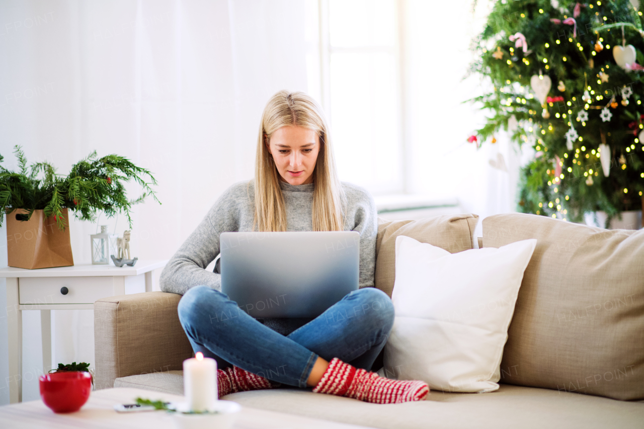 A young woman with laptop sitting on a sofa at home at Christmas time.