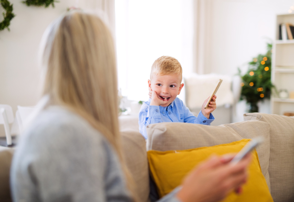 A mother and small boy with smartphones sitting on a sofa at home at Christmas time, playing games.