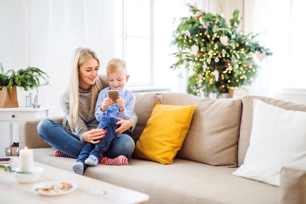 A mother and small boy with smartphone sitting on a sofa at home at Christmas time, playing games.