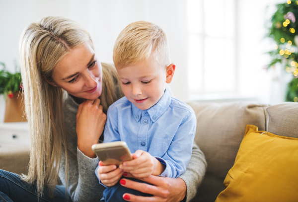 A mother and small boy with smartphone sitting on a sofa at home at Christmas time, playing games.