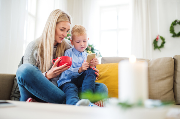 A mother and small boy with smartphone sitting on a sofa at home at Christmas time, playing games.