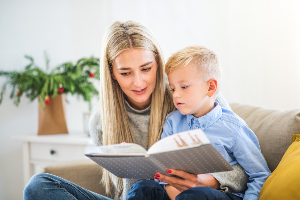 A mother and small boy sitting on a sofa at home at Christmas time, reading a story from a book.