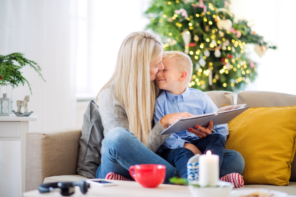 A mother and small boy sitting on a sofa at home at Christmas time, reading a story from a book.