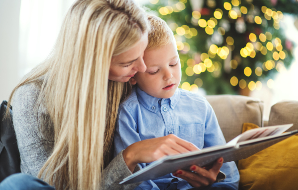 A mother and small boy sitting on a sofa at home at Christmas time, reading a story from a book.