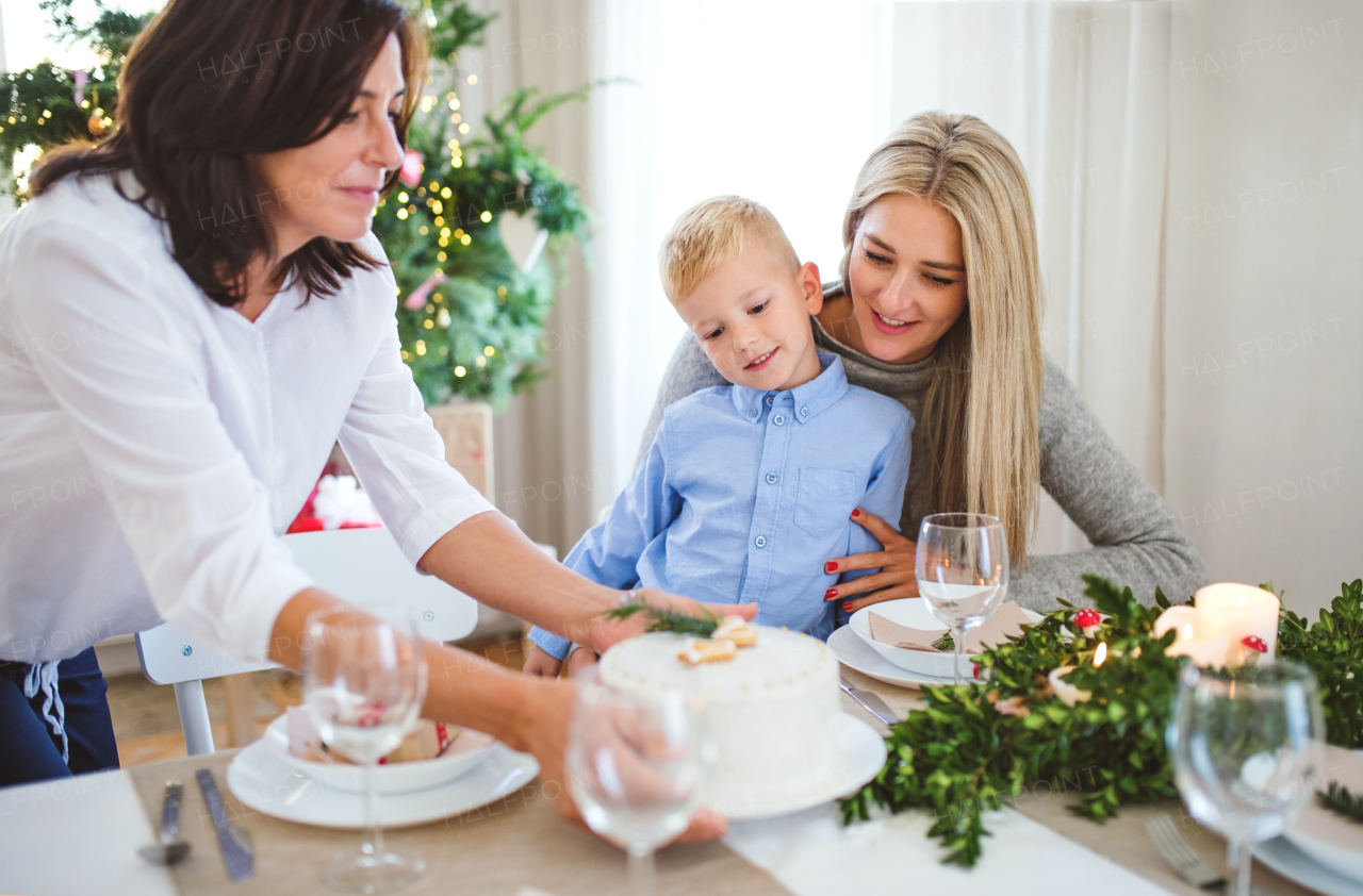 A small boy with motherlooking at grandmother putting a cake on table at home at Christmas time.