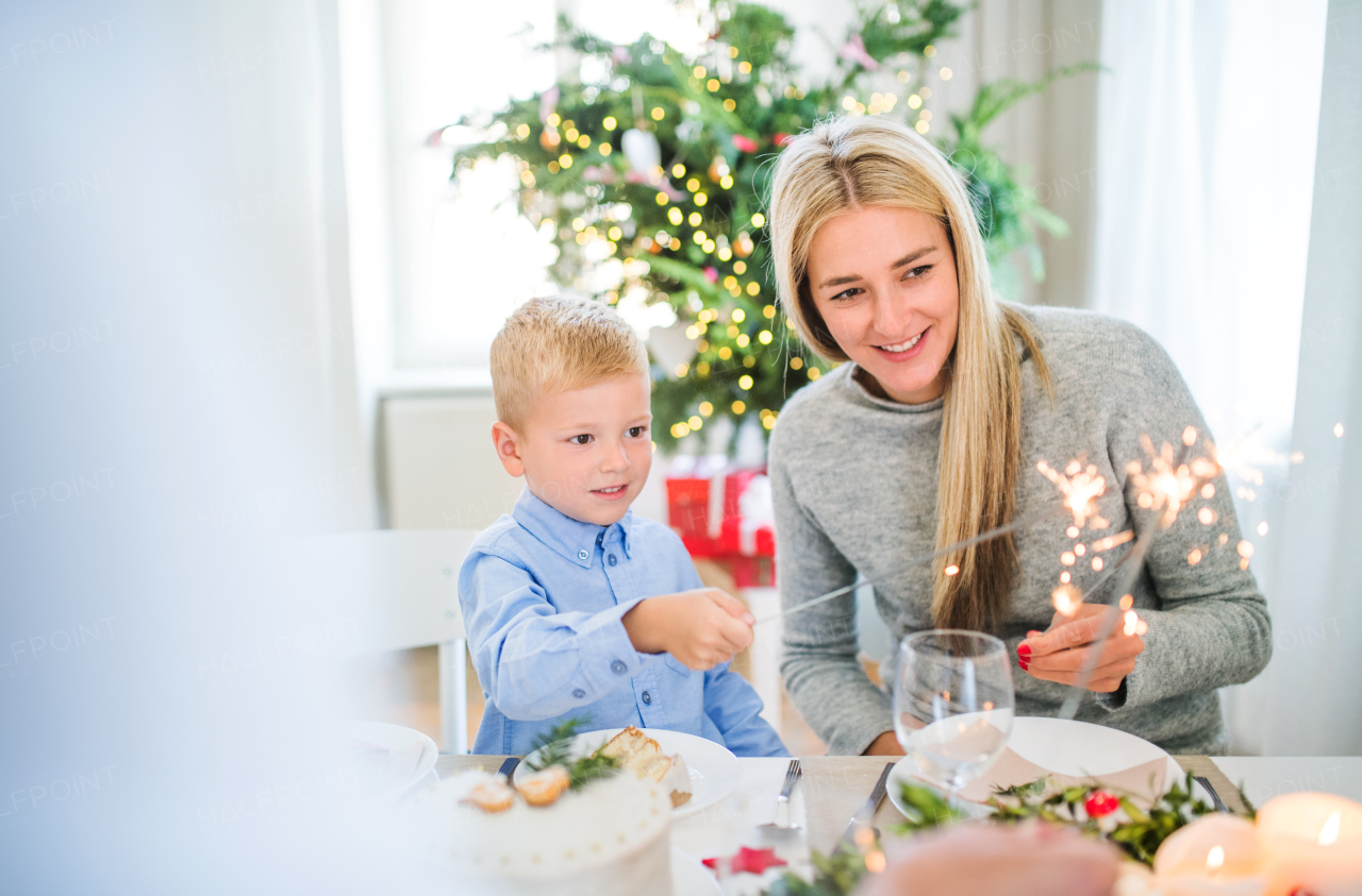 A small boy with mother sitting at a table at Christmas time, holding sparkles.